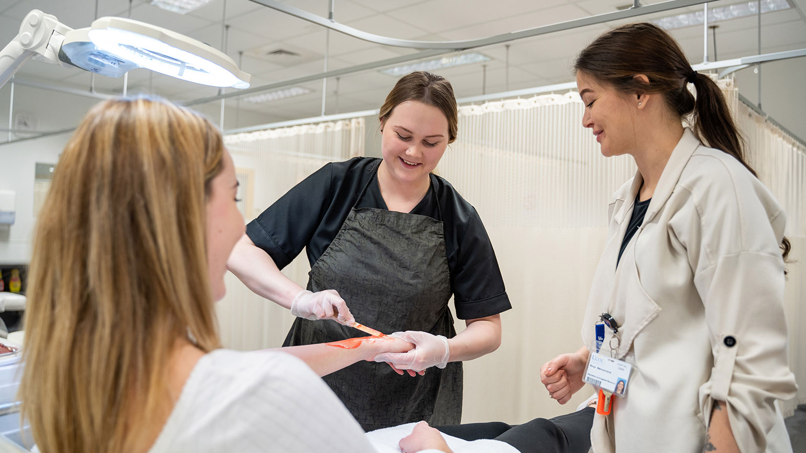 Two UCOL beauty students talking to a lecturer while working on a client